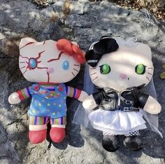 two hello kitty dolls sitting next to each other on a rock outside in the sun