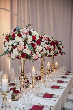 the table is set with white, red and pink flowers in tall gold vases