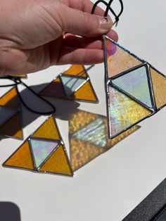 a hand is holding three stained glass pieces in the shape of triangulars on a white surface