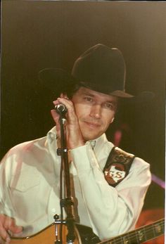 a man wearing a hat and holding a guitar in his right hand while standing next to a microphone