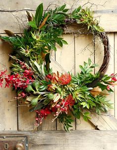 a wreath with red flowers and greenery hanging on a wooden door