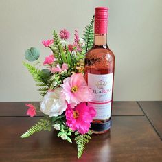 a bottle of wine sitting on top of a wooden table next to flowers and greenery