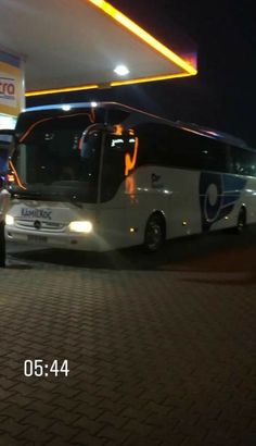 a white bus parked in front of a gas station at night with people standing around