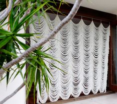 an open window with white curtains hanging from it's sides and palm trees in front