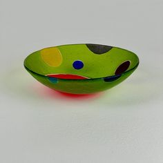 a green bowl with multi - colored dots on it sitting on a white table top