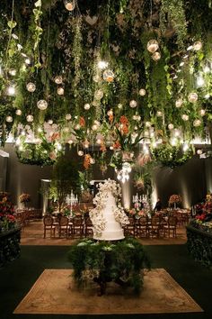 a wedding cake is surrounded by greenery and hanging lights