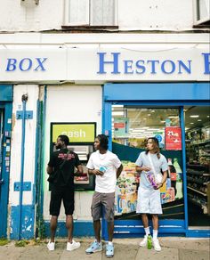 three people standing outside of a store with their hands in their pockets