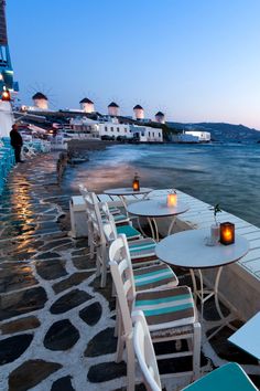 tables and chairs are lined up on the beach at dusk with lit candles in front of them