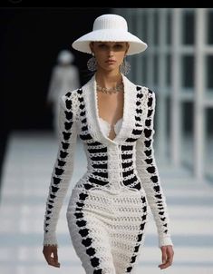 a woman walking down a runway wearing a white hat and black and white crochet dress