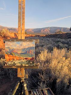 an easel with a painting on it sitting in the middle of a desert landscape