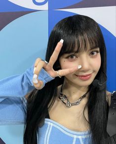 a girl with long black hair making the peace sign while standing in front of a blue and white wall