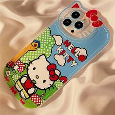 a cell phone case with hello kitty on the front and back cover, sitting on a satin surface