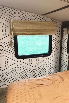 a bed sitting under a window next to a wall covered in black and white dots