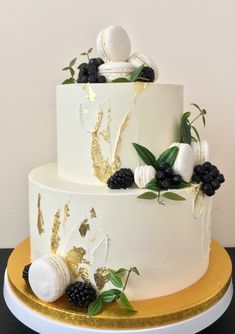 a three tiered white cake with blackberries and greenery