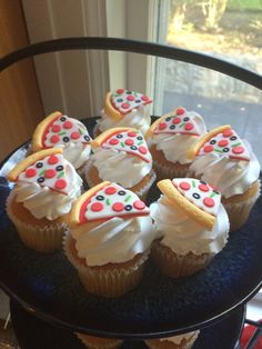 cupcakes with white frosting and colorful toppings on a black plate near a window