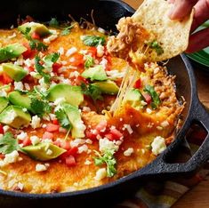 a person dipping tortilla into a skillet with salsa and avocado