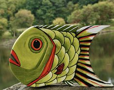 a green fish sculpture sitting on top of a rock near the water with trees in the background