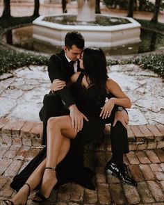 a man and woman sitting next to each other on a brick walkway in front of a fountain