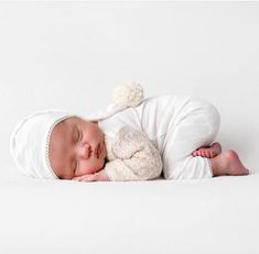 a newborn baby is sleeping with a stuffed animal in it's arms and wearing a white outfit