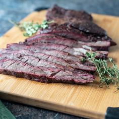 sliced up steak on a cutting board with herbs