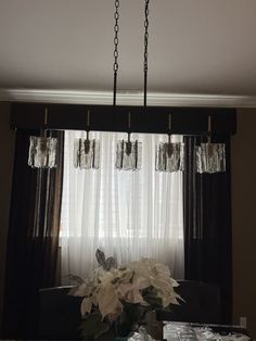 a vase with flowers in it sitting on a table next to a curtained window