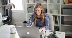 a woman sitting in front of a laptop computer on top of a white desk next to a plant