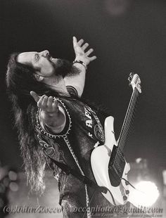 a black and white photo of a man with long hair playing an electric guitar on stage