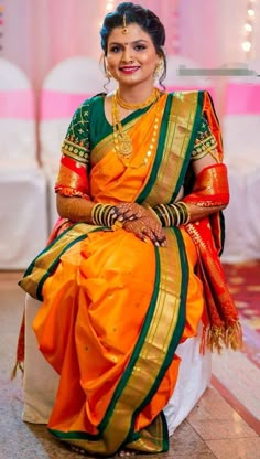 a woman in an orange and green sari sits on the floor with her hands clasped to her chest