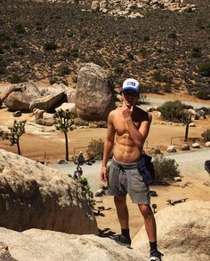 a shirtless man standing on top of a large rock in the middle of a desert