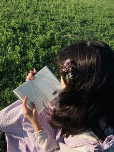 a woman reading a book in the middle of a green field with flowers on her head