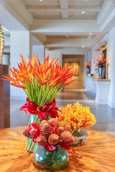 two vases filled with flowers sitting on top of a wooden table in a lobby