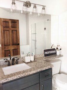 a white toilet sitting next to a bathroom sink under a mirror and light above it