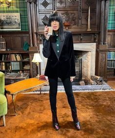 a woman taking a selfie in front of a fireplace wearing a suit and boots