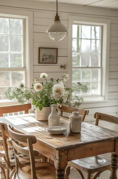 a wooden table topped with vases filled with flowers next to two chairs and a window