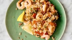 a green plate topped with rice and shrimp on top of a table next to a lemon wedge