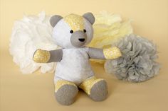 a teddy bear sitting next to some white and yellow flowers on a beige background with one flower in the foreground