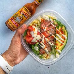 a person holding a plastic container with a salad in it next to a bottle of ketchup