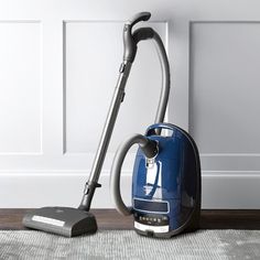 a blue vacuum is sitting on the floor next to a gray and white rug in front of a wall