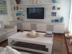 a living room filled with furniture and a flat screen tv mounted on a wall above a white coffee table