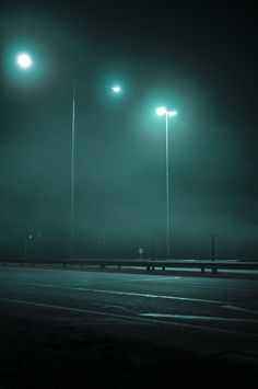 two street lights are lit up in the dark sky above an empty parking lot at night