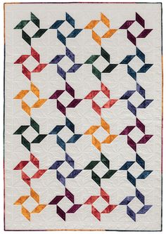 a quilt made with different colors and shapes on the side of a white wall hanging