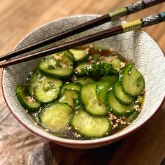 a bowl filled with sliced cucumbers and chopsticks on top of a wooden table