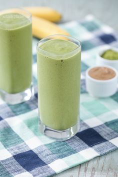 two glasses filled with green smoothie sitting on top of a checkered table cloth