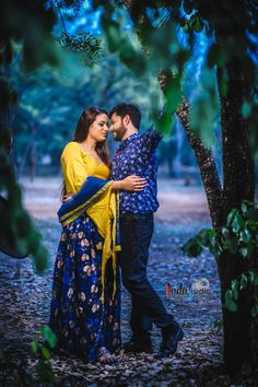 a man and woman standing next to each other under a tree in the middle of a forest