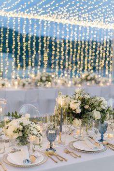 the table is set with white flowers, candles and place settings for an elegant dinner