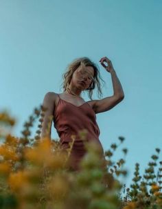 a woman in a brown dress standing on top of a hill with her hands behind her head