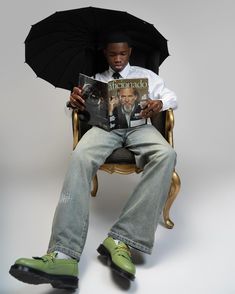 a man sitting in a chair with an umbrella over his head and reading a book