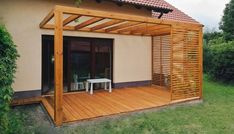 a wooden patio with an attached pergolan and table in the grass next to it