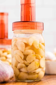 a jar filled with sliced bananas and garlic on top of a wooden table next to garlic cloves