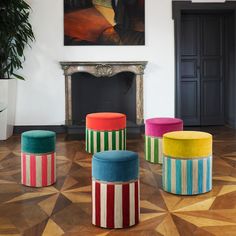 four colorful stools in front of a fireplace with a painting on the wall behind them